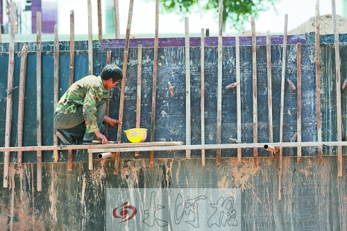 　　烈日下，狹窄的架子上，工人正用錘子固定樁基。