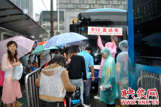 公交志愿者雨中高舉“B12-直達(dá)車”指示牌疏導(dǎo)返校學(xué)生乘車