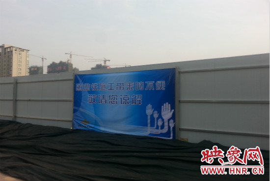 道路南側(cè)圍起了白色的圍擋，墻上標(biāo)示著“因地鐵施工帶來的不便敬請(qǐng)您諒解”的提示牌。