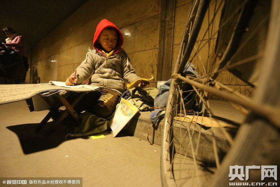 2015年11月8日晚，鄭州，7歲男孩涵洞橋下陪父母練攤，路邊燈下坐小馬扎上寫作業(yè)。