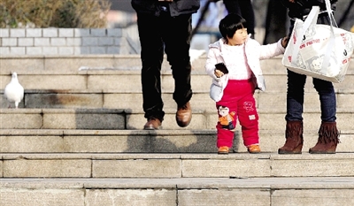 昨天中午，一女孩拉著家長(zhǎng)的手在紫荊山公園曬太陽，氣溫升高，孩子的棉衣解開了扣子。
